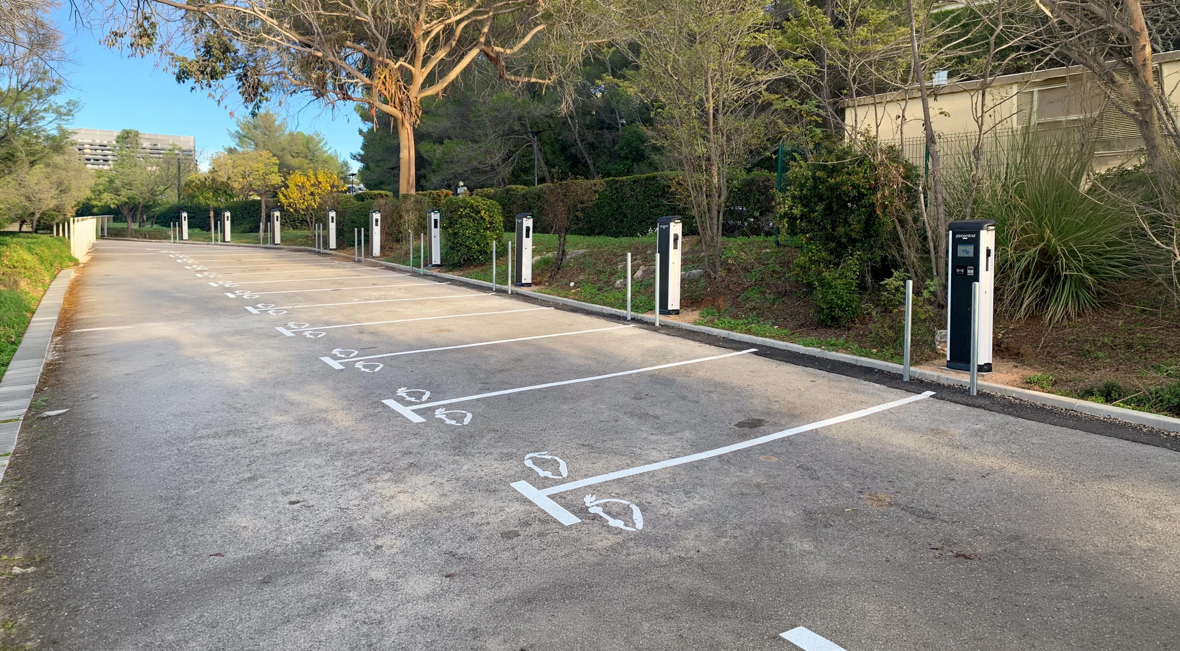 Parking extérieur vide équipé de bornes de recharge pour véhicules électriques, disposées en rangée sur toute la longueur